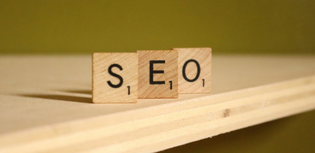 Wooden Scrabble pieces "S", "E", and "O" sit upright on a wooden shelf